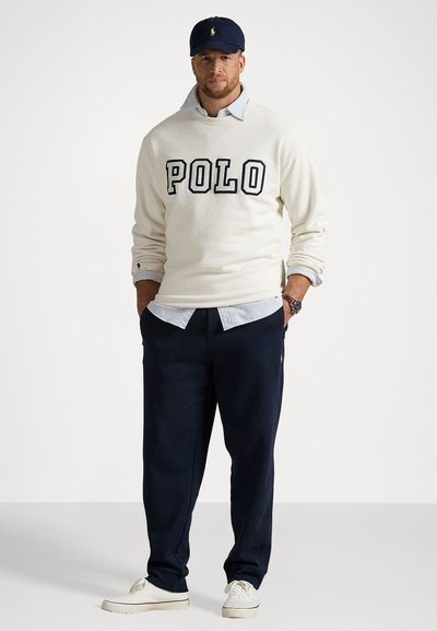 Bela mikica s "POLO" v mornarsko modrih črkah, prekrajana čez svetlo modro karirano srajco, v paru z mornarsko modrimi trenirkami in belimi športnimi copati.