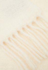 Crème-kleurige sjaal van zacht, fuzzy materiaal. Heeft franjes aan de randen en een subtiele gradient van wit naar lichtbeige.