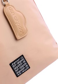 Bolso tote de nylon beige con una etiqueta de cuero con logotipo en relieve y una etiqueta negra con un diseño de texto repetido. Textura suave, forma moderna.