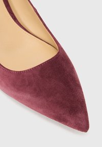 Burgundski pump z zazubljenim nosom, izdelan iz semiša, z gladko teksturo in nizkim izrezom na straneh za eleganten videz.