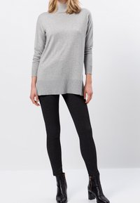 Túnica de punto gris con cuello alto y mangas largas, combinada con leggings negros texturizados y botas negras hasta el tobillo.