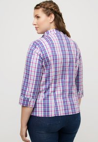 La camicia a quadri presenta motivi in viola, rosa e bianco, con un collo alto e maniche a tre quarti. Il tessuto appare liscio con una leggera lucentezza.