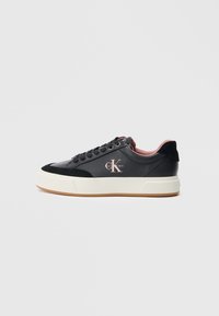 Sapatilha preta com parte superior em couro liso, detalhes em camurça, pormenores rosa claro e uma sola branca espessa. Apresenta atacadores redondos e logotipo.