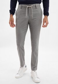 Pantaloni grigi su misura con una trama sottile, cintura regolabile con coulisse e tasche inclinate, abbinati a sneakers bianche sportive.