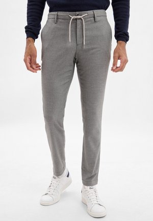 Pantaloni grigi su misura con una trama sottile, cintura regolabile con coulisse e tasche inclinate, abbinati a sneakers bianche sportive.