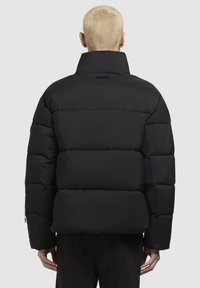 Schwarze Daunenjacke mit hohem Kragen, gestepptem Design und sichtbaren Nähten. Sie hat eine kastige Silhouette und seitliche Reißverschluss-Taschen.