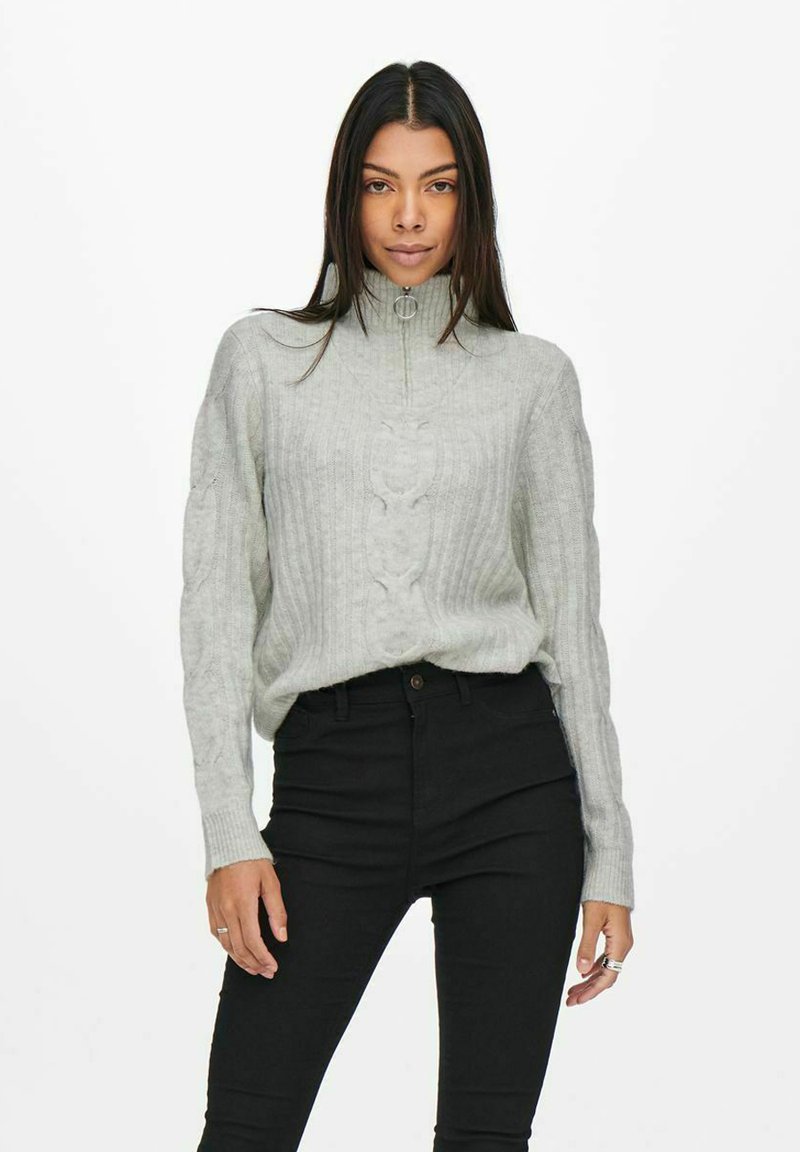 Light grey knitted sweater with a high collar, ribbed texture, front cable detailing, and long sleeves, paired with black high-waisted pants.