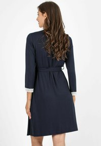 Accappatoio blu navy con maniche lunghe, cintura in vita e bordo in pizzo ai polsini. Il tessuto morbido scivola delicatamente fino a un'altezza a metà coscia.
