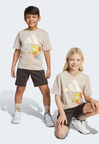 Camisetas beige con un personaje de dibujos animados y un logo blanco, combinadas con pantalones cortos oscuros y zapatillas blancas. Los calcetines tienen un diseño de dibujos animados.