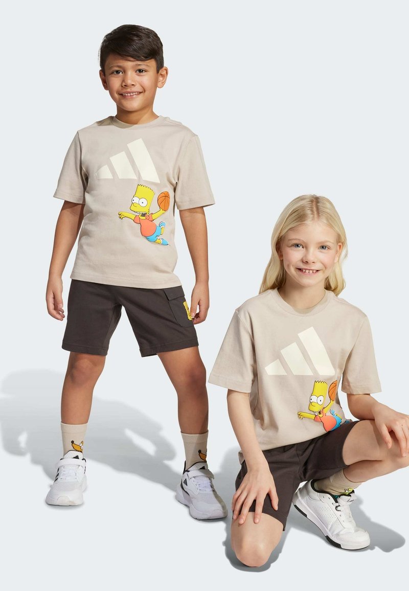 Camisetas beige con un personaje de dibujos animados y un logo blanco, combinadas con pantalones cortos oscuros y zapatillas blancas. Los calcetines tienen un diseño de dibujos animados.