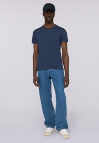 Námořnická modrá bavlněná trička spojená se světle modrými džíny. Oblečení obsahuje tmavou čepici a krémové tenisky, čímž vytváří ležérní vzhled.