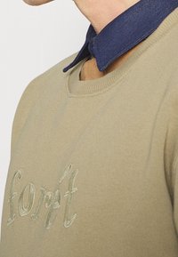 Oliwkowa bluza z haftowanym napisem "forêt", z granatowym denimu kołnierzem, okrągłym dekoltem i ściągaczami na rękawach.