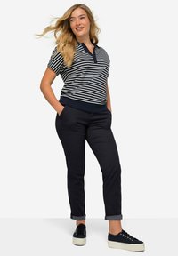 Polo a righe blu navy e bianche con scollo a V, abbinato a pantaloni slim-fit blu navy scuri e sneakers nere con suola bianca.