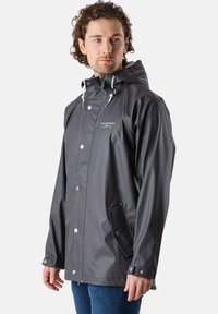 Veste de pluie imperméable grise avec capuche, boutons-pression, cordons réglables et poches latérales. Texture lisse avec un design moderne.