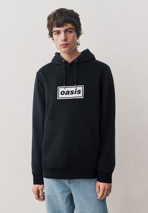 Musta huppari, jossa on etukangurutasku ja valkoinen "oasis"-logo. Hupussa on kiristysnauhat, ja hihansuut sekä helma ovat resorilliset. Yhdistetty vaaleansinisiin farkkuihin.