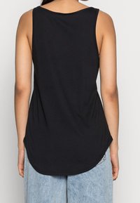 Black sleeveless top with a rounded neckline, made from soft fabric. Features a curved hem and loose fit. Worn with light blue wide-leg jeans.