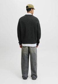 Mørkegrå strikket sweater med en løs pasform, parret med lysegrå vidde bukser, og en grøn kappe; en ensfarvet hvid skjorte nedenunder.