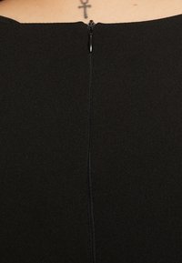 Prenda negra con una tela suave y texturada que cuenta con una cremallera vertical en la parte posterior. Diseño minimalista sin patrones ni acentos visibles.