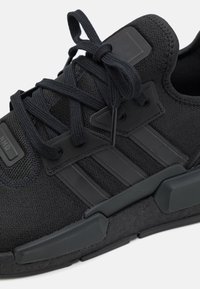 Zapatilla deportiva negra con parte superior de tela texturizada, cordones planos, tres franjas horizontales y suela de goma con un diseño moldeado.