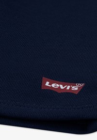Πλεκτό ύφασμα σε ναυτικό μπλε με ραβδωτή υφή, που διαθέτει εύθυρη κόκκινη ετικέτα με το λογότυπο Levi's σε λευκό χρώμα στο κάτω δεξιό μέρος.