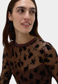 Průhledný hnědý top s černou květinovou výšivkou, kulatým výstřihem a úzkým střihem. Černé korálkové náušnice s detaily ve tvaru střapce.