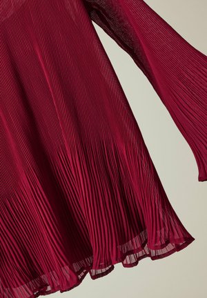 Robe plissée en bordeaux profond, dotée d'un tissu texturé avec des manches longues et un ourlet fluide, soulignant le mouvement du design.