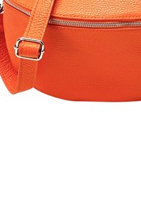 Ronde, oranje leren crossbody tas met een textuurafwerking, voorzien van een zilveren rits en een verstelbare schouderband.