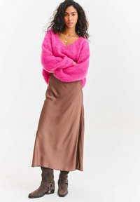 Ružový nadýchaný pletený sveter s výstrihom do V a dlhými rukávmi, v kombinácii s hnedou saténovou sukňou s trakmi. Sivé vysoké čižmy po kolená so sponami.