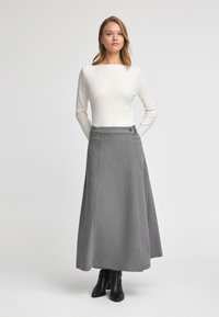 Grå knälång kjol i ett robust tyg, med sidoknappar och en slät yta. Matchas med en figurnära vit topp.