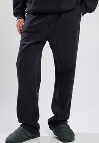Pantalones de chándal negros hechos de tejido suave, con un corte relajado, cintura texturizada, bolsillos laterales y un discreto detalle de logo en la pierna.