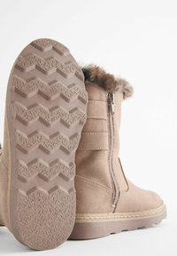 Botines marrones de ante con suela de goma texturada que presenta un patrón de zigzag, cremallera lateral y borde de pelaje sintético alrededor de la abertura.