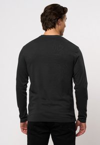 Tricou din bumbac negru cu mânecă lungă, cu guler rotund, având o textură netedă și un design minimalist. Fără logo-uri sau grafică vizibile.