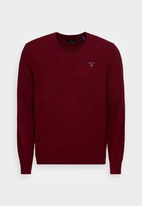 Pull en V maroon pour homme avec des manches longues, des poignets et un ourlet côtelés, arborant un petit logo blanc GANT sur la poitrine gauche.
