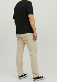 Svart kortärmad t-shirt, ljusbeige raka jeans och svarta sneakers. Jeans har bakfickor, enkel design och minimal dekoration.