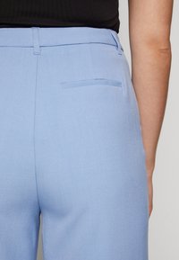 Svetle modré látkové kalhoty s hladkou zadní kapsou, hladkým povrchem a přiléhavým střihem, s čistým pasem a jemnými detaily v švech.