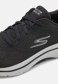 Sneaker nere con una tomaia in rete testurizzata, lacci robusti, dettagli riflettenti e una suola imbottita di colore bianco sporco, con un logo argentato.