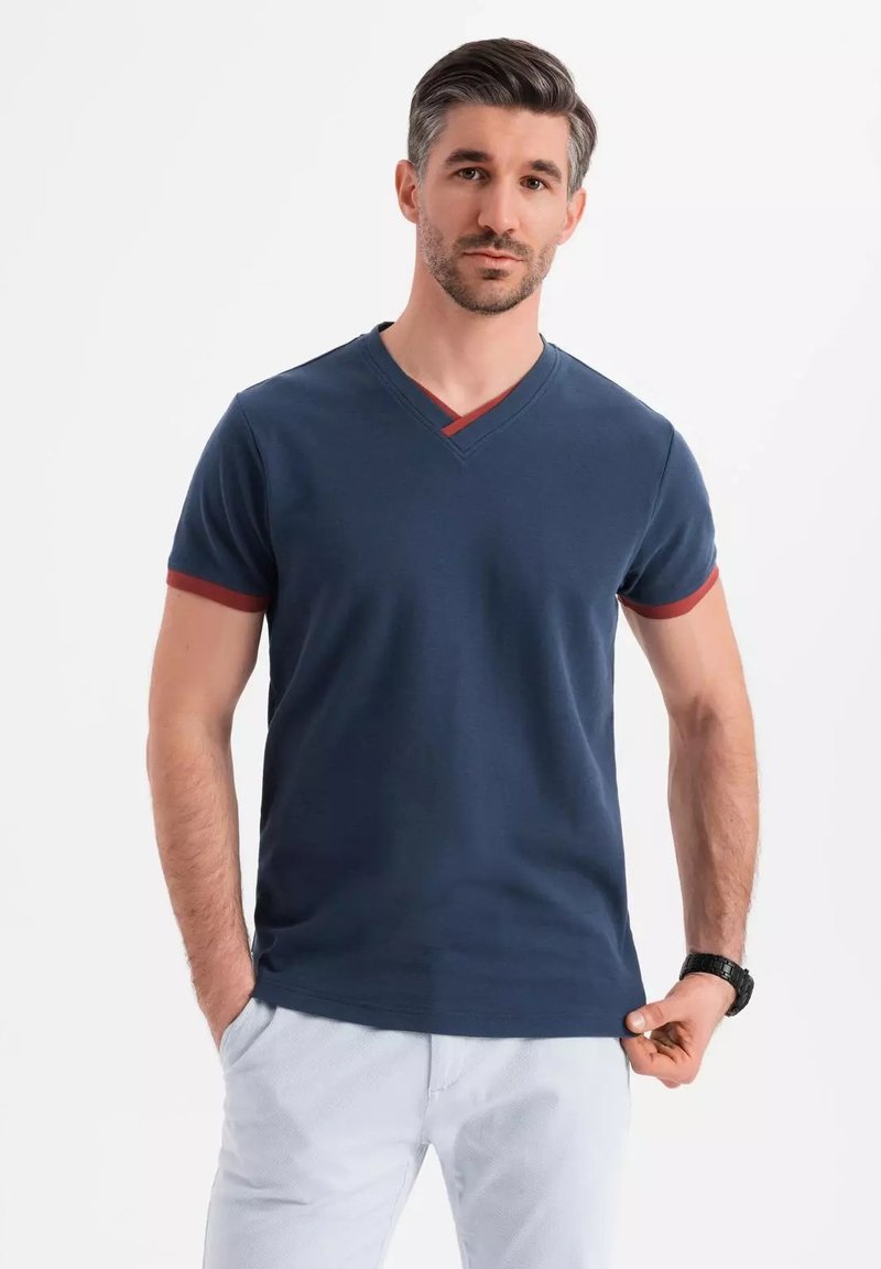 Camiseta de v cuello azul marino con acentos rojos en el cuello y los dobladillos de las mangas, fabricada en un tejido suave; diseño ajustado, mangas cortas.