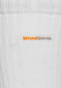 Weiße Baumwollsocke mit vertikaler Rippstruktur und einem horizontalen Muster aus orangefarbenen und grauen Streifen nahe der Oberkante. Weicher Stoff.