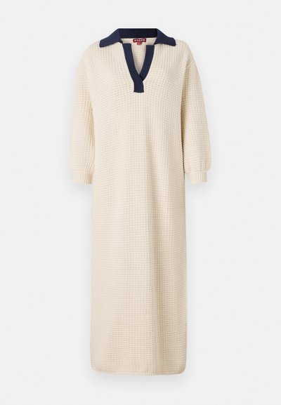 Rochie lungă, de culoare crem, cu un material texturat, având un guler bleu marin și un design cu decolteu în V. Mâneci clopot de trei sferturi completează aspectul.