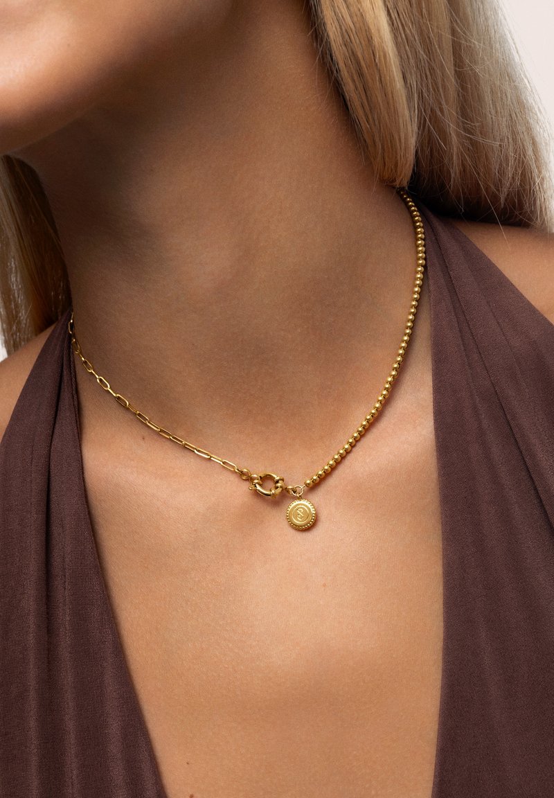 Goldene Halskette mit einer Kombination aus Kugelketten- und Gliederkettenabschnitten, mit einem runden Anhänger, der ein erhabenes Design zeigt.