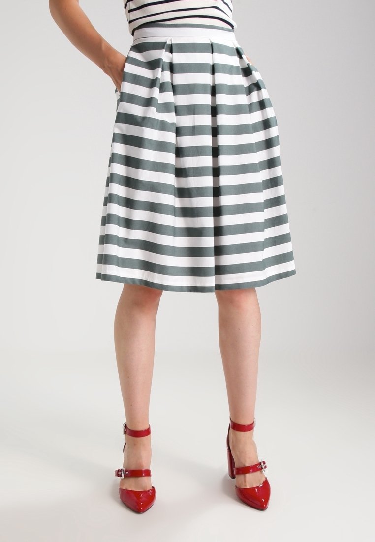 Randig kjol med gröna och vita toner, plisserad design och sidofickor. Matchad med glansiga röda högklackade skor med vristremmar.