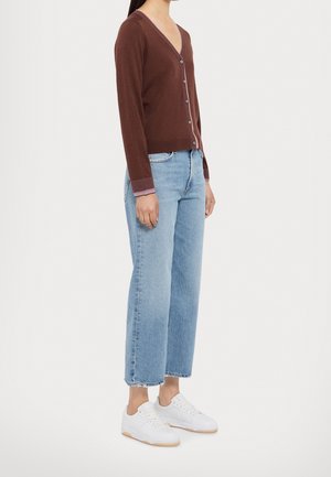 Cardigan marron tricoté avec un col en V, devant boutonné et poignets rayés contrastants, associé à un jean large bleu clair et des baskets blanches.