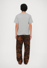 T-shirt grigia in cotone e pantaloni cargo marroni con motivo, caratterizzati da un collage di immagini con accenti neri su un tessuto testurizzato.