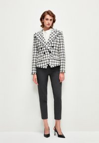 Chaqueta de cuadros en blanco y negro con solapas de muesca, usada sobre una blusa blanca y combinada con pantalones de sastre en color carbón y tacones negros.