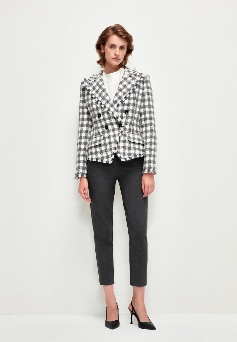 Chaqueta de cuadros en blanco y negro con solapas de muesca, usada sobre una blusa blanca y combinada con pantalones de sastre en color carbón y tacones negros.
