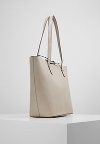 Lysebeige tote bag lavet af glat læder, med forlængede håndtag, minimalistisk design og en subtil kontrastsyning langs kanterne.
