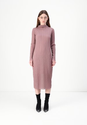 Ribbed knit, long-sleeve dress in soft mauve with high neckline and midi length. Worn with black ankle socks and pointed-toe heels.
