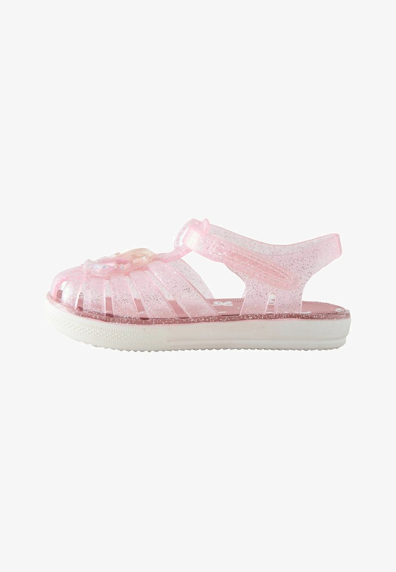 Sandale translucide rose pour tout-petit avec paillettes, bout fermé, décoration florale et bride de cheville réglable sur semelle blanche.