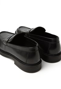 Schwarze, glänzende Slipper mit runder Zehenpartie, gesteppten Akzenten und einer flachen Gummisohle. Offenes Rückendesign für einfachen Einstieg.