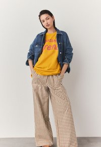 Giacca di jeans con grandi tasche, maglietta gialla con testo rosa e pantaloni larghi a quadri marroni con vestibilità morbida.